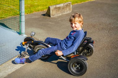 Küçük bir yolda üç tekerlekli bisiklet süren bir çocuk