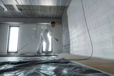 Man in overall painting an industrial wall with white acrylic paint clipart