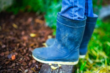 Lastik çizmeli ve kot pantolonlu çocuk bahçeye yakın.