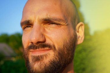 Güneşli bir günde sakallı ve bıyıklı yakışıklı bir adamın portresi.