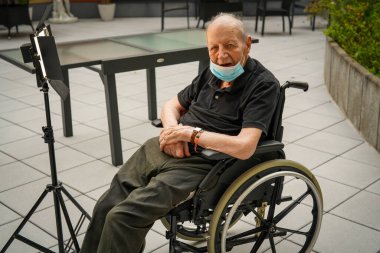 Yaşlı adam tekerlekli sandalyede oturuyor ve Covid-19 salgını sırasında maske takıyor.