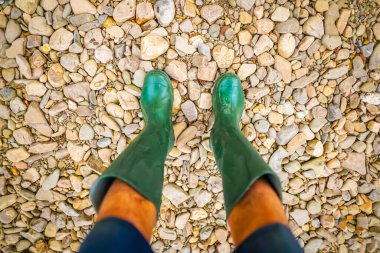 Ayakları çakıllı yeşil yağmur botları giyen bacaklar.