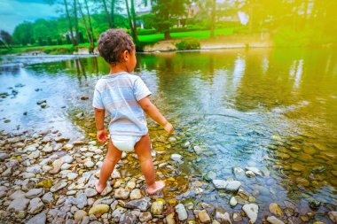2 yaşındaki melez Afrikalı çocuk nehir kıyısında çakıl taşlarıyla oynuyor.
