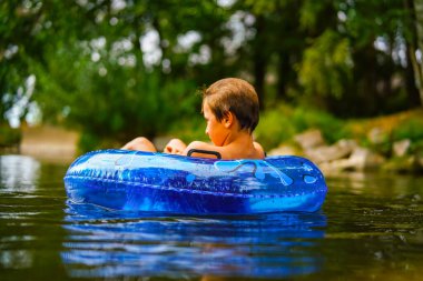 Vahşi bir nehirde, mavi bir şamandırada yalnız bir çocuk dinleniyor.