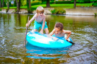 Nehirde mavi şişme şamandırada oynayan çocuklar