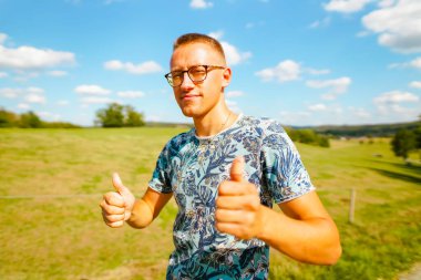 Yaz tarlasında baş parmak gösteren genç adam. 