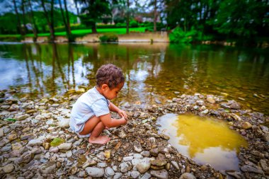 2 yaşındaki melez Afrikalı çocuk nehir kıyısında çakıl taşlarıyla oynuyor.