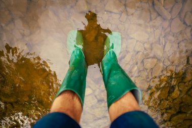 Yeşil lastik çizmeli adam nehirde duruyor. 