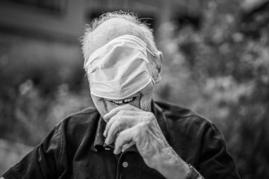 Gözlerine maske takmış yaşlı bir adamın portresi ve Covid-19 salgını sırasında gülümsüyor.