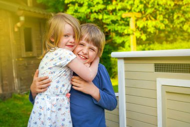 Genç bir oğlan ve kız bahçede tavuk kümesinin yanında oynuyorlar.