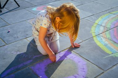 Küçük kız asfalta tebeşir çiziyor. 