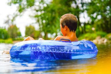 Vahşi bir nehirde, mavi bir şamandırada yalnız bir çocuk dinleniyor.