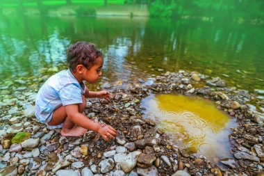 2 yaşındaki melez Afrikalı çocuk nehir kıyısında çakıl taşlarıyla oynuyor.