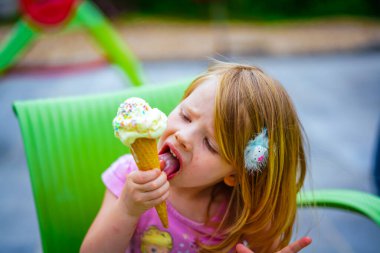 Parkta dondurma yiyen küçük tatlı bir kızın portresi.