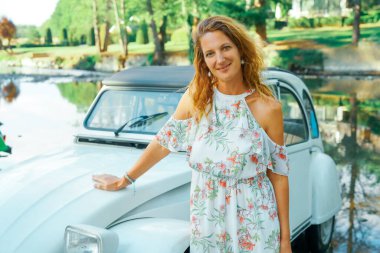 ROCHEFORT, BELGIUM - AUGUST 10, 2020: Old antique Citroen 2cv vintage car near a river in a forest with young smiling woman wearing a white dress in the Belgian countryside