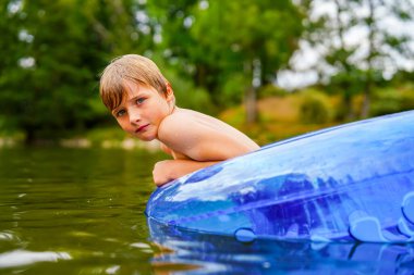 Vahşi bir nehirde, mavi bir şamandırada yalnız bir çocuk dinleniyor.