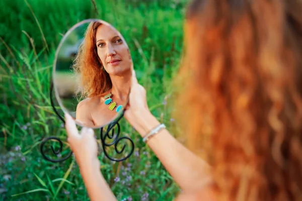 年轻的红头发女人举着一面圆圆的小镜子 看着自己的倒影 怀旧地看着自己 — 图库照片