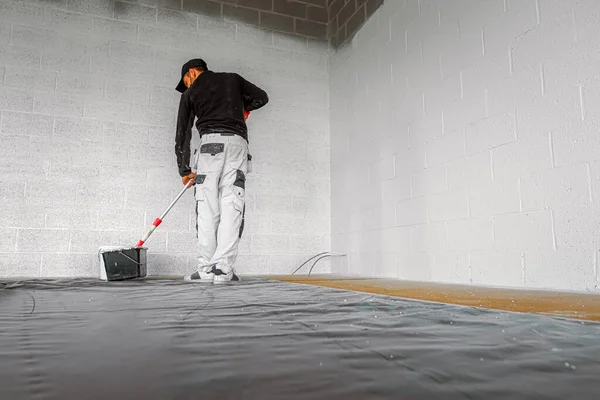 Man in overall painting an industrial wall with white acrylic paint