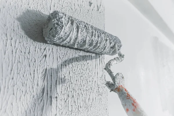 Wall being plastered and painted in white with roller and thick paint in unfinished building