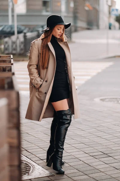 Jeune femme élégante en manteau beige avec un chapeau noir dans une rue de la ville. Mode de rue féminine. Vêtements d'automne.Style urbain — Photo