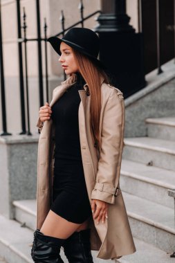 Şehir caddesinde siyah şapkalı, bej ceketli şık genç bir kadın. Kadın sokak modası. Sonbahar giysileri. Şehir tarzı..