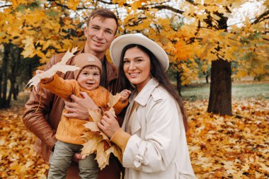 Anne ve baba ve oğul sonbahar parkında yürüyorlar. Altın sonbaharda bir aile doğa parkında yürüyor..