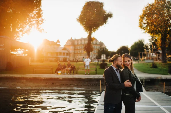 Una familia de dos personas se encuentra en un muelle en el casco antiguo de Austrias al atardecer. Un hombre y una mujer se abrazan en el terraplén de un pequeño pueblo en Austria.Europea.Felden am Werten see — Foto de Stock