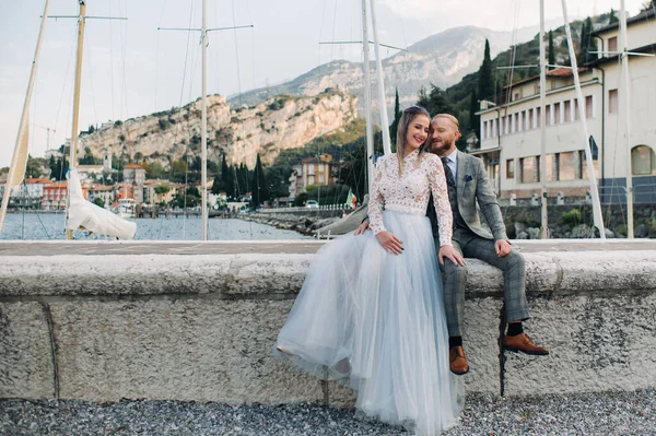 Italia, Lago de Garda. Una hermosa pareja a orillas del lago de Garda en Italia a los pies de los Alpes. Un hombre y una mujer se sientan en un muelle en Italia —  Fotos de Stock