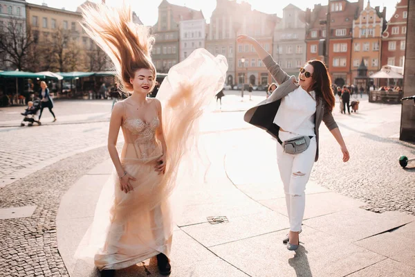 Una chica lanza un vestido de novia a una novia con el pelo largo en el casco antiguo de Wroclaw. Sesión de fotos de boda en el centro de una antigua ciudad en Polonia.Wroclaw, Polonia — Foto de Stock
