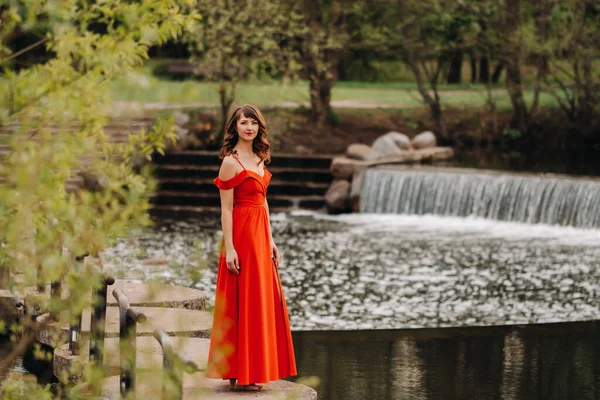 Дівчина в довгій червоній сукні біля озера в парку на заході сонця . — стокове фото