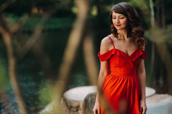 Una giovane bella ragazza con lunghi capelli castani, in un abito lungo rosso con un anello intorno al lago — Foto Stock
