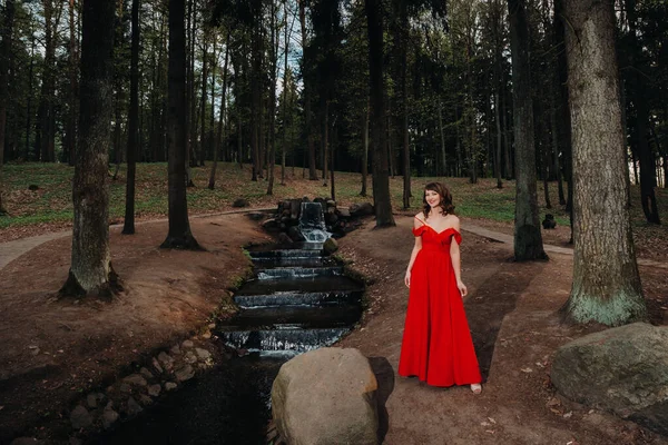 Primavera Retrato de una niña riendo en un largo vestido rojo con el pelo largo caminando en el parque en el bosque — Foto de Stock