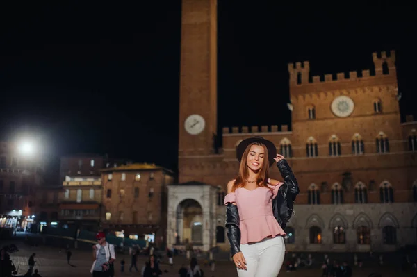 En flicka i hatt går genom nattstaden Siena i Toscana.En flicka går runt i staden i Italien.Toscana. — Stockfoto