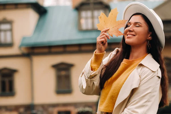 Una chica con un abrigo blanco y un sombrero sonríe en un parque otoñal.Retrato de una mujer en otoño dorado. —  Fotos de Stock