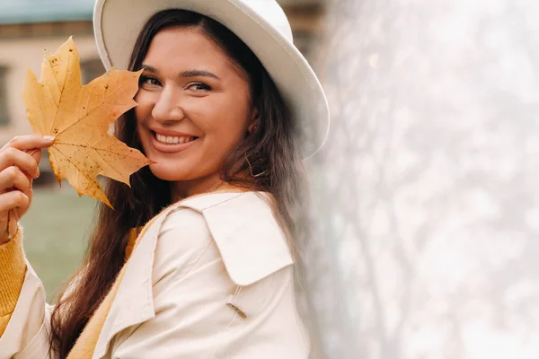 Ein Mädchen in weißem Mantel und Hut lächelt in einem herbstlichen Park.Porträt einer Frau im goldenen Herbst. — Stockfoto