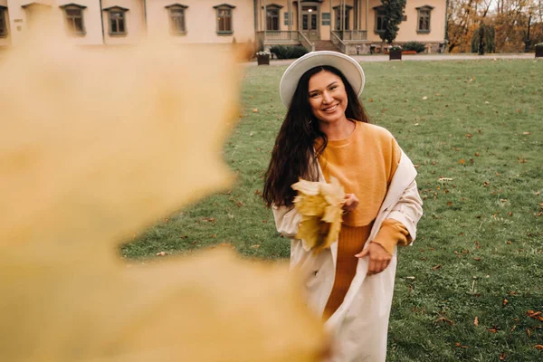 Ein Mädchen in weißem Mantel und Hut lächelt in einem herbstlichen Park.Porträt einer Frau im goldenen Herbst. — Stockfoto