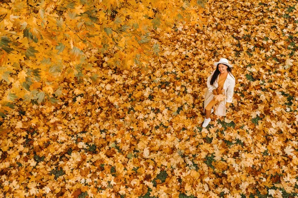 Ein Mädchen in weißem Mantel und Hut lächelt in einem herbstlichen Park.Porträt einer Frau im goldenen Herbst. — Stockfoto