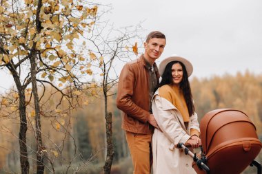 Annem ve babam sonbahar parkında bebek arabasıyla yürüyüşe çıktılar. Aile, altın sonbaharda doğa parkında yürür..