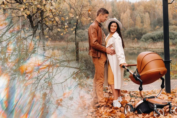 Père et mère en promenade avec une poussette dans le parc d'automne. La famille se promène dans le parc naturel à l'automne doré. — Photo