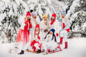 Velká skupina dívek s lízátkem v rukách stojí v zimním lese.Dívky v červených a bílých šatech s cukrovinkami ve sněhem pokrytém lese