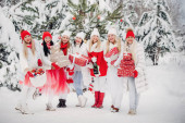 Velká skupina dívek s vánočními dárky v rukou stojící v zimním lese.Dívky v červených a bílých šatech s vánočními dárky ve zasněženém lese.
