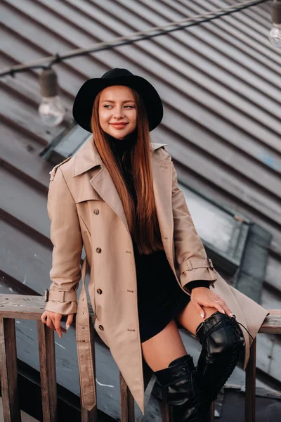 Stylish Young Woman Beige Coat Black Hat Sits Rooftop City — Stock Photo, Image