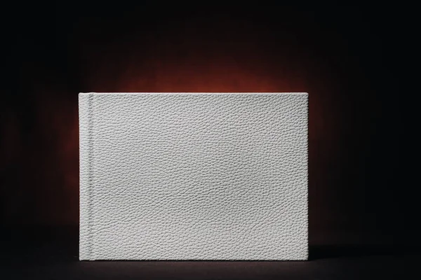 White book in genuine white leather on a dark embossed background . White paper on a dark background