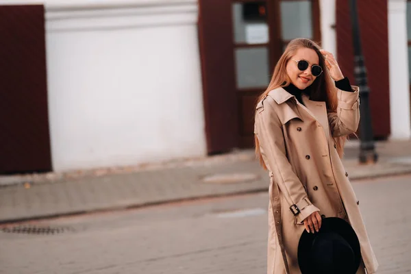 ベージュのコートを着たスタイリッシュな若い女性と 街の通りで彼の手と眼鏡に黒い帽子 女性のストリートファッション Urban Style — ストック写真