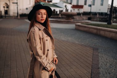 Şehir caddesinde siyah şapkalı, bej ceketli şık genç bir kadın. Kadın sokak modası. Sonbahar giysileri. Şehir tarzı..