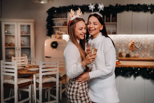 Dos chicas en un ambiente acogedor en casa con champán en sus manos en Navidad. Las chicas sonrientes beben champán en una velada festiva —  Fotos de Stock