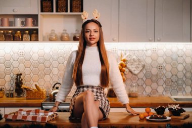 Noel 'de geyik boynuzları olan bir kız mutfak masasına oturur ve gülümser..