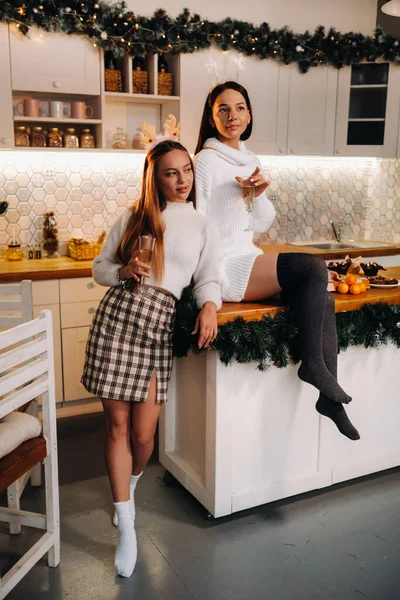 两个女孩在舒适的家庭环境中在厨房里 手里拿着香槟酒过圣诞节 在节日的夜晚 微笑的女孩们喝着香槟 — 图库照片