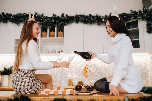 两个女孩在舒适的家庭环境中在厨房里为圣诞节倒香槟 在节日的夜晚 微笑的女孩们喝着香槟 — 图库照片