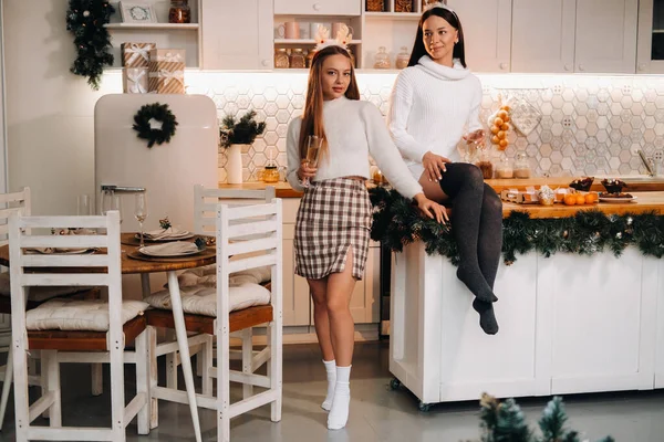 两个女孩在舒适的家庭环境中在厨房里 手里拿着香槟酒过圣诞节 在节日的夜晚 微笑的女孩们喝着香槟 — 图库照片